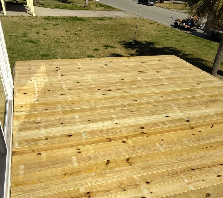 Newly built ground-level pressure-treated deck beside a home